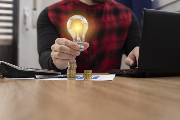 mao de negocios segurando lampadas com laptop e dinheiro empilhados no escritorio conceito de economia de energia e financas contabeis na luz da manha 188913 94