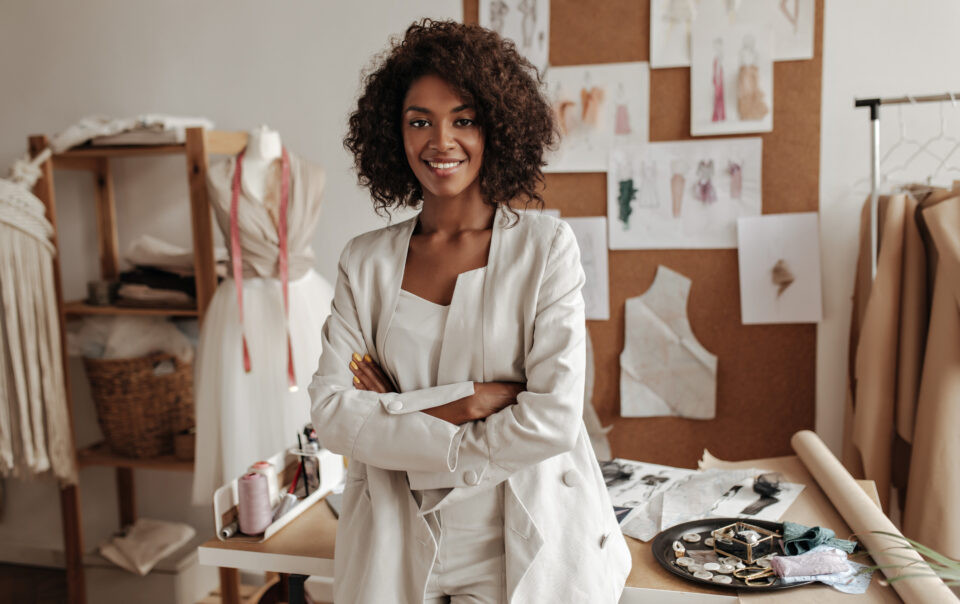 beautiful curly brunette dark skinned fashion designer poses in office leans on table