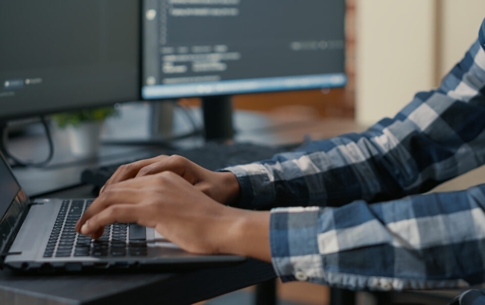 closeup of programer hands typing machine learning code on laptop keyboard in front of computer screens with programming interface system engineer writing algorithm for online cloud computing