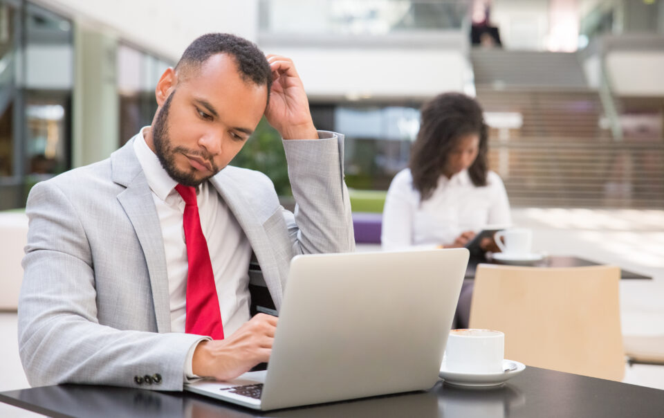 pensive male manager using laptop while drinking coffee