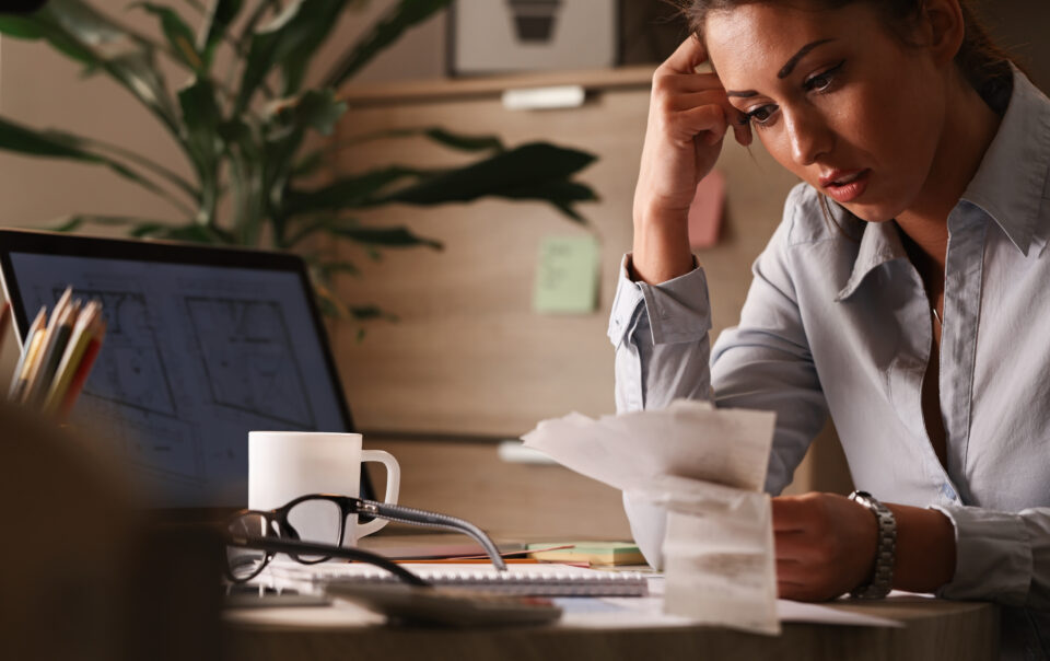 businesswoman feeling worried about financial debts analyzing bills while working office