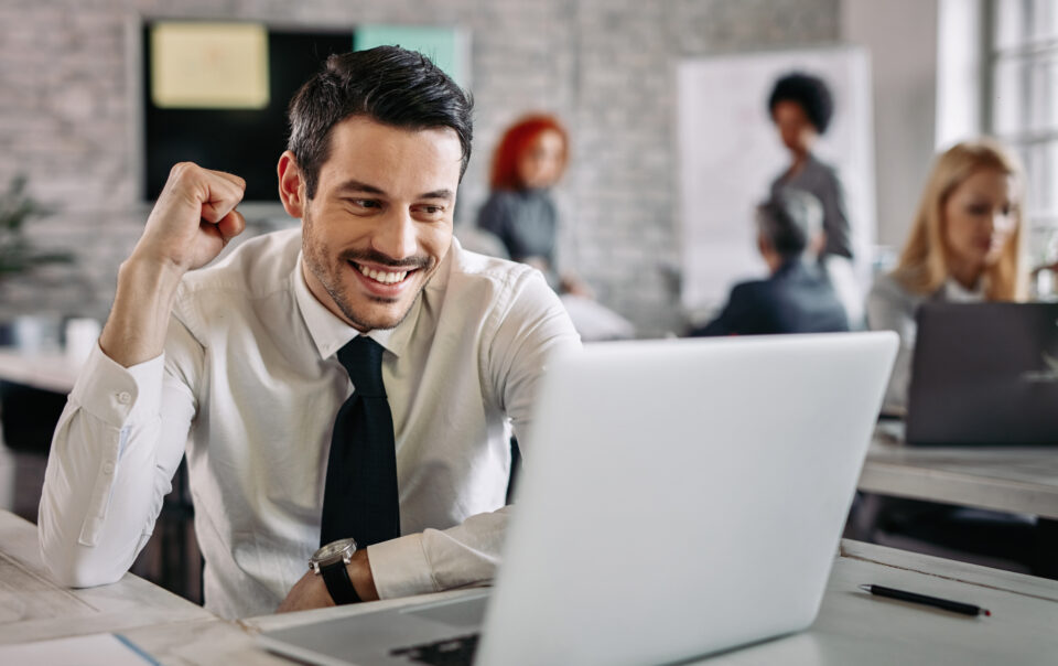 young happy businessman using computer office celebrating good news there are people background