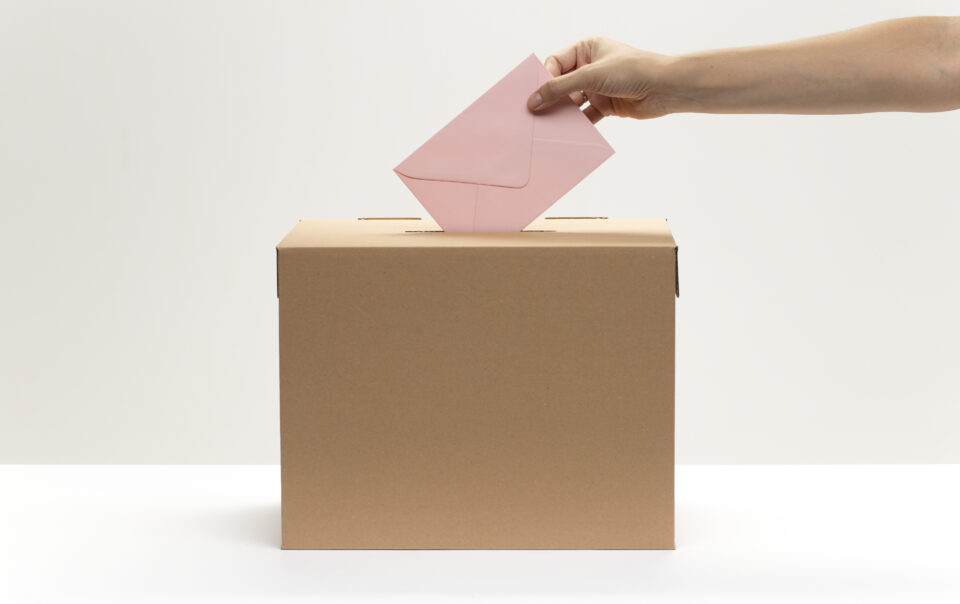 hand puts pink envelope into vote box