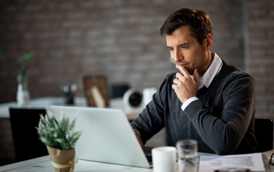 smiling businessman using laptop contemplating while working his desk office