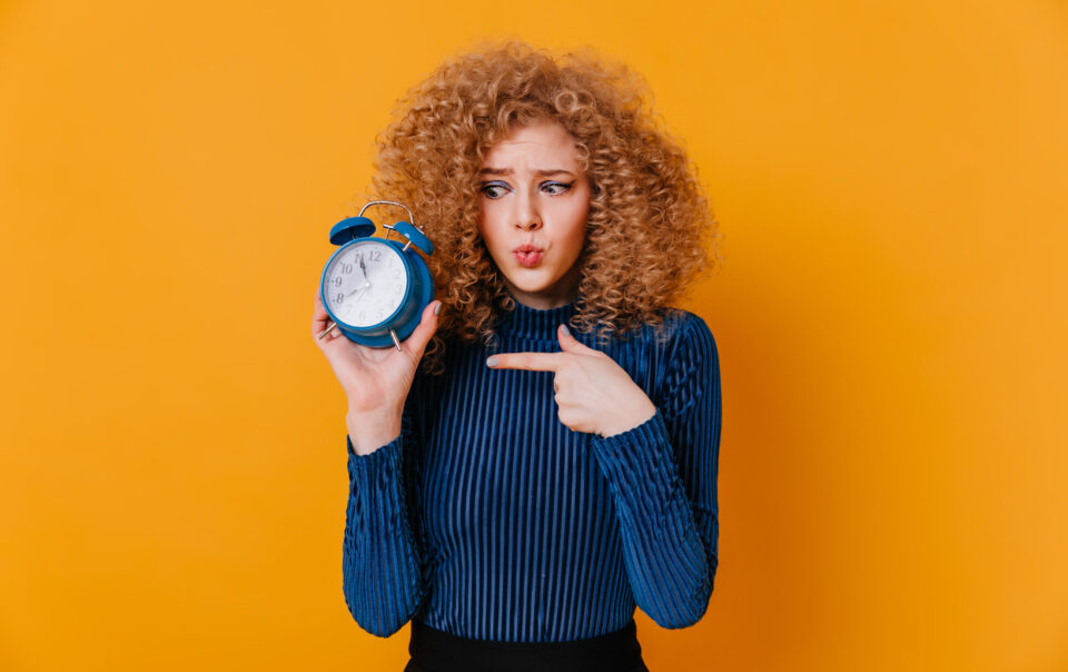 curly girl blue striped sweater looks alarm clock with suspicion points finger it