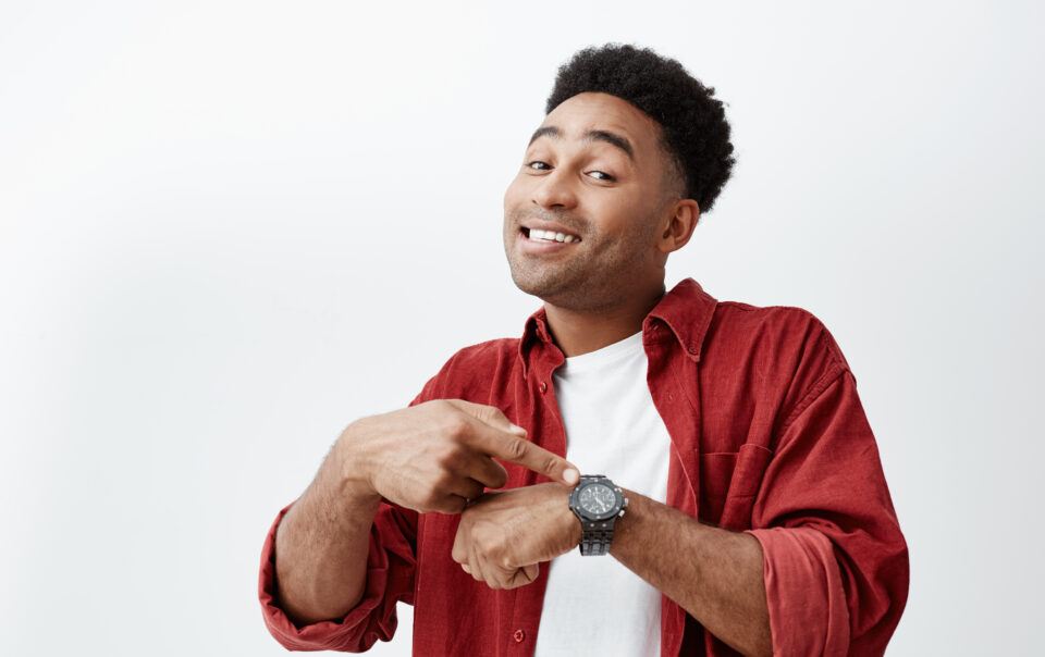 what time is it portrait young attractive dark skinned man with dark afro hairstyle white t shirt red shirt pointing hand watch with happy face expression showing it time eat